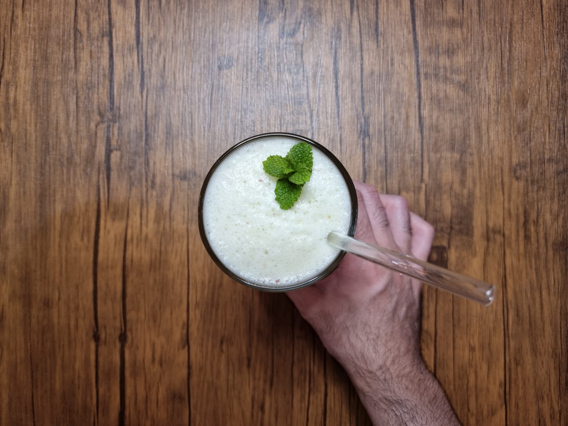 Foto do suco pronto, decorado com uma folha de hortelã e com um canudo de vidro dentro do copo.